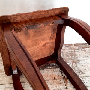 Peut inclure: Un tabouret en bois brun fonc&eacute; avec une assise carr&eacute;e et des pieds incurv&eacute;s. Le dessous de l'assise est visible, montrant le grain du bois et la construction. Le tabouret semble &ecirc;tre vintage ou antique.