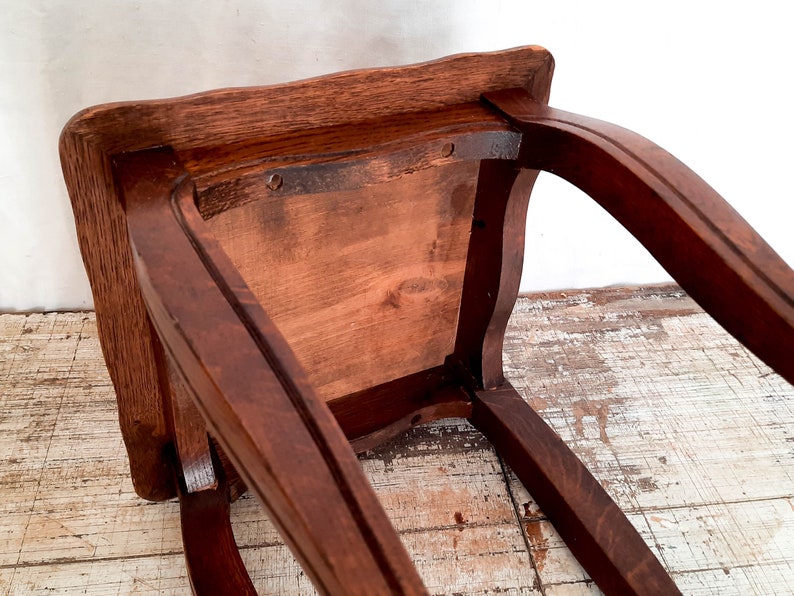 Peut inclure: Un tabouret en bois brun fonc&eacute; avec une assise carr&eacute;e et des pieds incurv&eacute;s. Le dessous de l'assise est visible, montrant le grain du bois et la construction. Le tabouret semble &ecirc;tre vintage ou antique.