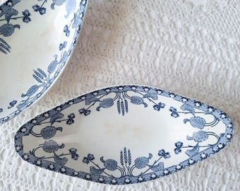 May include: Two oval-shaped ceramic dishes featuring a white base with a blue transferware pattern of stylized floral motifs and wheat stalks. The edges of the dishes are decorated with a repeating blue and white botanical border design.