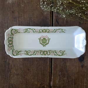 Puede incluir: Una bandeja rectangular blanca para servir con un borde floral verde y rosa. El centro de la bandeja presenta un diseño floral verde y rosa con un monograma en el centro.