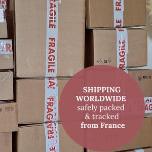 Peut inclure: Plusieurs bo&icirc;tes en carton marron empil&eacute;es, scell&eacute;es avec du ruban adh&eacute;sif blanc portant l'inscription "FRAGILE" en rouge. L'image contient le texte "SHIPPING WORLDWIDE safely packed & tracked from France."