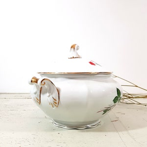 May include: White porcelain soup tureen with a gold trim and floral design. The tureen has a lid with a gold knob and a handle on each side.