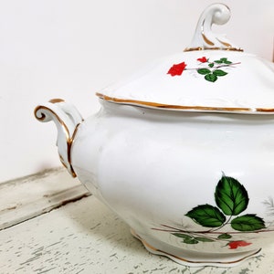 May include: White porcelain soup tureen with a lid and gold trim. The tureen is decorated with a red rose and green leaves.