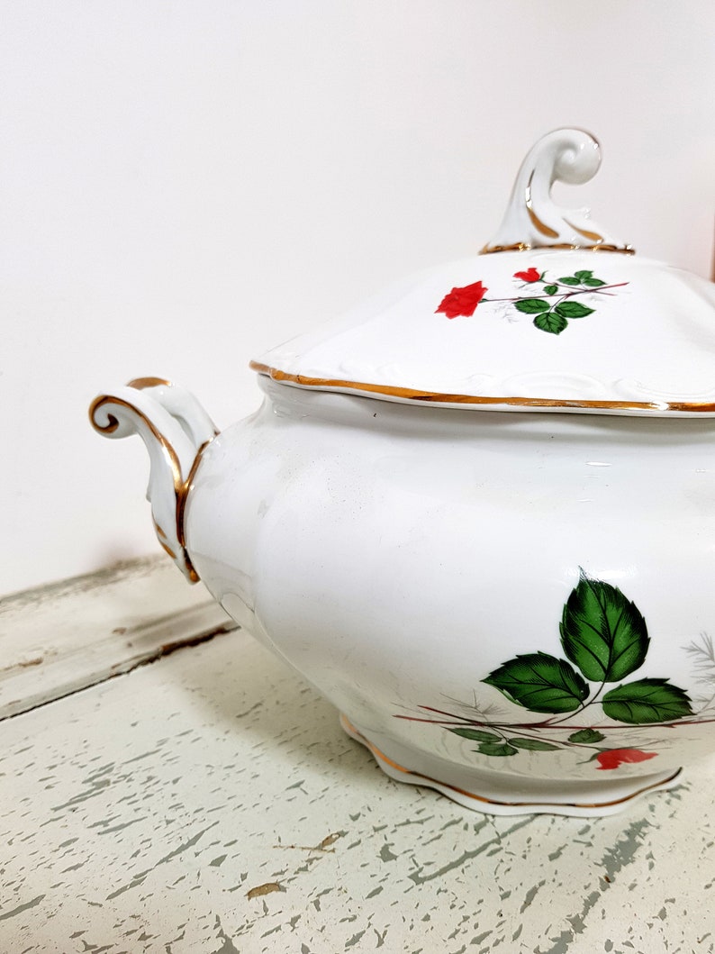 May include: White porcelain soup tureen with a lid and gold trim. The tureen is decorated with a red rose and green leaves.