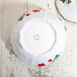 May include: White porcelain bowl with a red rose design. The bowl has a scalloped edge and a gold trim. The bottom of the bowl is marked "Porcelaine Fine" and "Made in France".