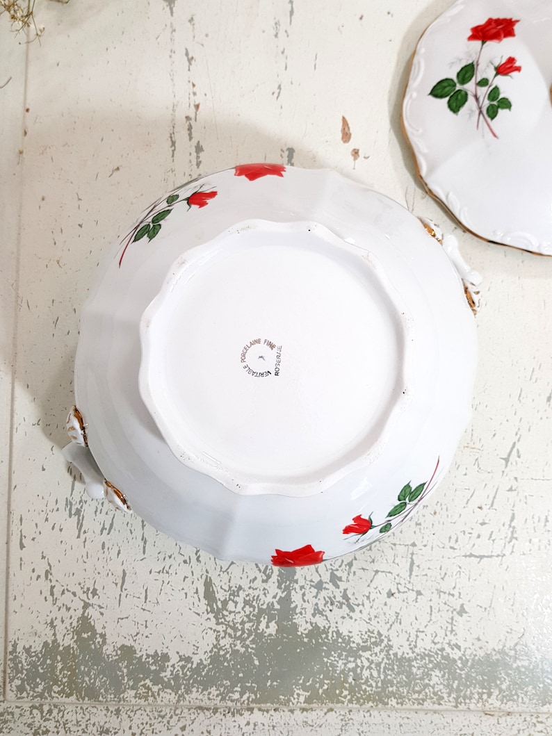 May include: White porcelain bowl with a red rose design. The bowl has a scalloped edge and a gold trim. The bottom of the bowl is marked "Porcelaine Fine" and "Made in France".