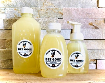 May include: Three bottles of foaming hand soap with honey and essential oils. The bottles are labeled "BEE GOOD" and feature a bee logo. The bottles are clear and the soap is a light yellow color.