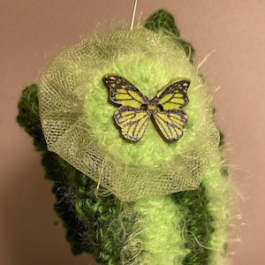 May include: A green and light green crocheted headband with a fuzzy texture and a wooden butterfly embellishment.
