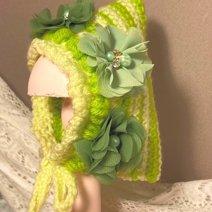 May include: A green and yellow striped crocheted baby hat with green fabric flowers and pearl embellishments.
