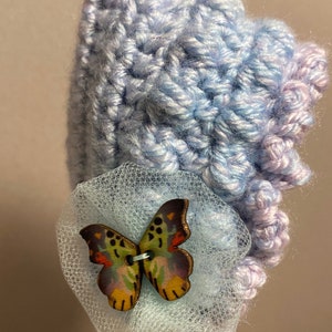 May include: A light blue crocheted baby hat with a light blue tulle bow and a wooden butterfly embellishment.