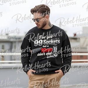 Puede incluir: Sudadera negra con el texto "I've got 99 Sockets but a 10mm ain't one" y un gráfico de herramientas. El diseño incluye un juego de llaves de vaso, una llave de vaso y un vaso. La sudadera es usada por una persona.