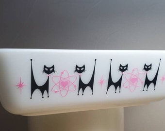 May include: White ceramic baking dish with a black and pink design of stylized cats and atomic symbols.