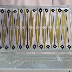 May include: A vintage glass baking dish with a lid. The dish has a black and gold geometric pattern with stars.