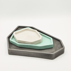 May include: Three geometric concrete trays in different sizes. The largest tray is gray, the middle tray is light blue, and the smallest tray is off-white.