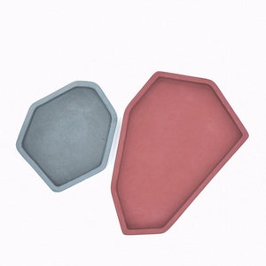 May include: Two geometric concrete trays, one gray and one red, with a slightly irregular shape.