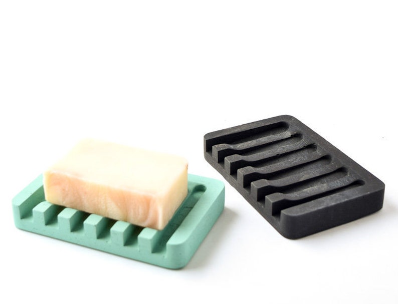 May include: Two soap dishes, one green and one black, with a bar of soap in the green dish. Both dishes have a ridged design to help drain water.