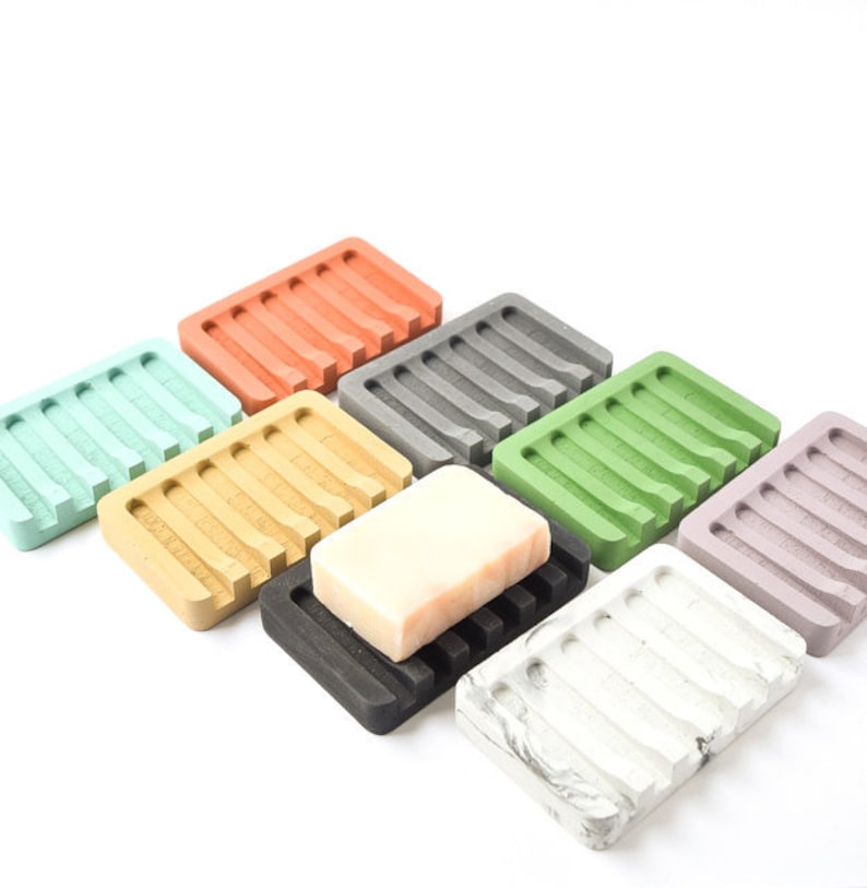 May include: Assortment of ten soap dishes in various colors, including orange, gray, green, beige, black, white, and purple. The dishes are made of a textured material and have a raised design. One dish has a bar of soap on top.