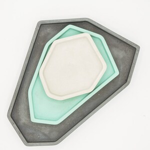 May include: Three geometric trays, one gray, one light green, and one white, are stacked on top of each other. The trays are all hexagonal in shape and have a smooth, polished finish.