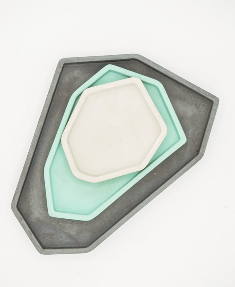 May include: Three geometric trays, one gray, one light green, and one white, are stacked on top of each other. The trays are all hexagonal in shape and have a smooth, polished finish.