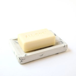 May include: A white soap dish with a marble pattern and a bar of soap that says "ALL ONE" on it.
