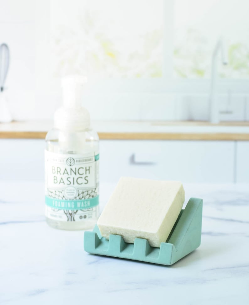 May include: A light green soap dish with a white bar of soap inside. A bottle of Branch Basics foaming wash is in the background.