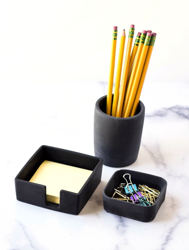 K&ouml;nnte beinhalten: Schwarzes Schreibtisch-Organizer-Set mit drei F&auml;chern. Das Set beinhaltet einen Stiftehalter, einen Notizblockhalter und eine kleine Schale f&uuml;r B&uuml;roklammern. Der Stiftehalter ist mit gelben Bleistiften gef&uuml;llt.