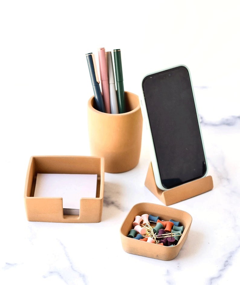 K&ouml;nnte beinhalten: Ein Set aus vier Schreibtisch-Organizern aus Terrakotta. Das Set enth&auml;lt einen Stiftehalter, einen Telefonst&auml;nder, einen Notizblockhalter und eine kleine Schale f&uuml;r Stecknadeln und B&uuml;roklammern. Die Organizer sind alle in einem hellen Braunton gehalten.