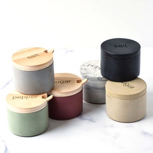 May include: Set of six small, round, ceramic containers with wooden lids. The lids have a small wooden spoon attached. The containers are labeled "salt", "pepper", "sugar", "salt", "pepper", and "sugar".