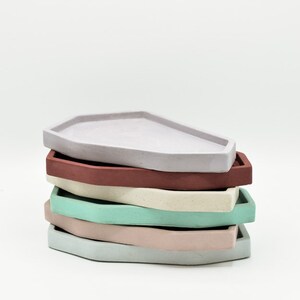 May include: A stack of five geometrically shaped concrete trays in various pastel colors, including light purple, red, cream, light green, and pink.