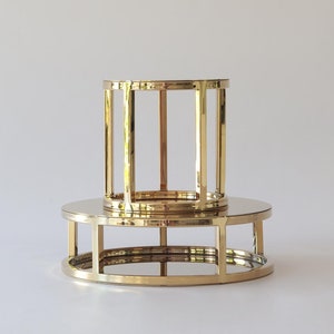 May include: A two-tiered gold metal cake stand with a round top and bottom. The stand is made of thin metal bars that create a cage-like design.