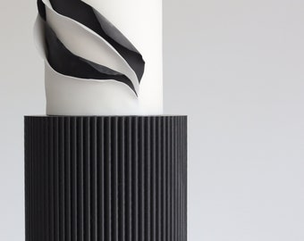 May include: A three-tiered wedding cake with black and white fondant. The top tier has a white fondant base with a black and white abstract design. The middle tier is black fondant with vertical lines. The bottom tier is white fondant.