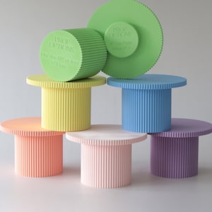 Könnte beinhalten: Sechs pastellfarbene runde Tortenständer mit geriffelten Kanten. Die Ständer sind pyramidenförmig gestapelt. Der oberste Ständer ist grün und hat den Text "PROP OPTIONS 8" Top Plate Base 5"+" aufgedruckt. Der zweite Ständer ist gelb, der dritte blau, der vierte orange, der fünfte rosa und der sechste lila.