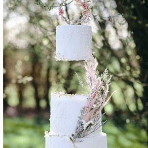 Peut inclure: Un gâteau de mariage blanc à trois étages avec des accents de feuilles d'or et des fleurs séchées. Le niveau supérieur est suspendu à une branche avec une couronne florale.