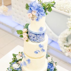 May include: A four-tier wedding cake decorated with blue and white flowers. The cake is topped with a topper that says "Mr. & Mrs."