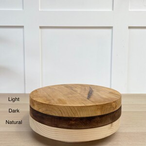 May include: Three round wooden cake stands stacked on top of each other. The top stand is light wood, the middle stand is dark wood, and the bottom stand is natural wood.