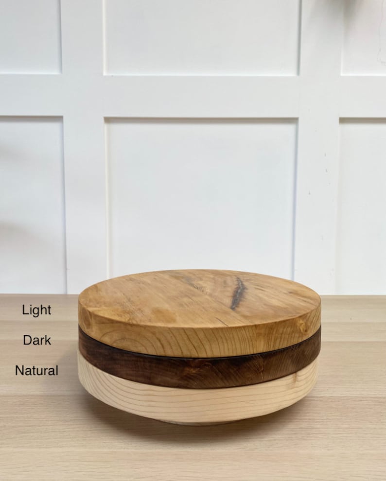 May include: Three round wooden cake stands stacked on top of each other. The top stand is light wood, the middle stand is dark wood, and the bottom stand is natural wood.