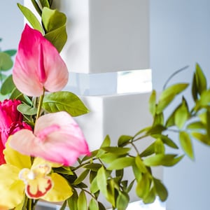 Może przedstawiać: Biały kwadratowy tort ślubny z przezroczystymi akrylowymi warstwami ozdobionymi różowymi i żółtymi kwiatami oraz zielonymi liśćmi.