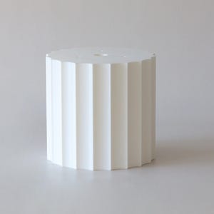 Puede incluir: Un pedestal cilíndrico blanco con un diseño acanalado. El pedestal tiene una parte superior lisa y redondeada y una base ligeramente más ancha.