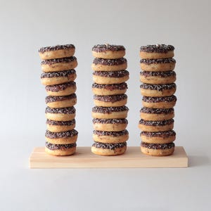 Pode incluir: Três pilhas de donuts cobertos de chocolate com granulado numa tábua de madeira. Cada pilha tem 10 donuts.