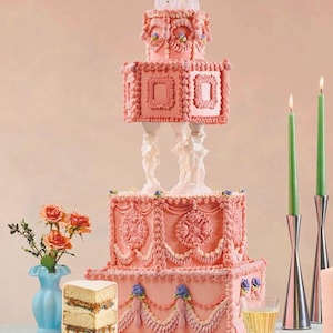 Puede incluir: Una tarta de boda rosa de varios niveles con intrincados detalles de glaseado, incluyendo diseños florales y de volutas. La tarta está coronada con una figura de novios. Se ve una porción de tarta, junto con velas verdes y un jarrón azul con flores.