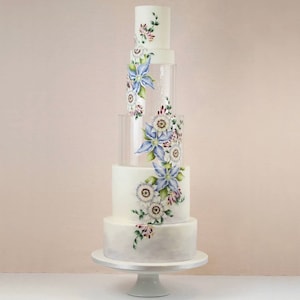 May include: A white wedding cake with clear acrylic tiers decorated with hand-painted floral designs in shades of blue, white, and green.