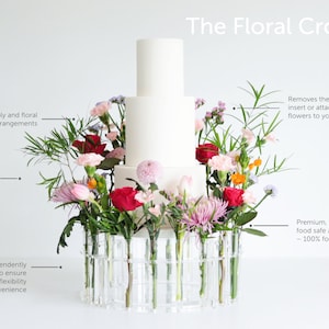May include: A white cake sits on a clear acrylic floral crown with a variety of flowers in pink, red, and white. The text "The Floral Crown" is at the top of the image. The crown is made of clear acrylic tubes that hold the flowers. The text "Removes the need to insert or attached fresh flowers to your cake" is on the right side of the image. The text "Premium, ultra-polished food safe acrylic - 100% food safe" is also on the right side of the image.