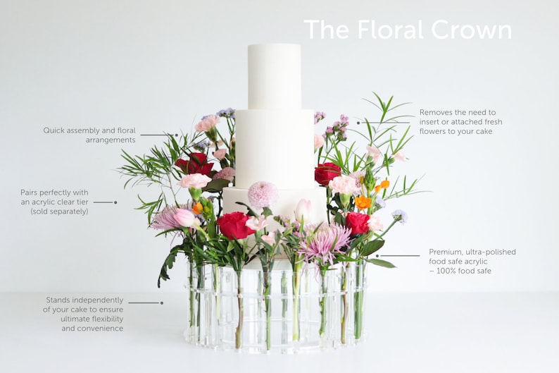 May include: A white cake sits on a clear acrylic floral crown with a variety of flowers in pink, red, and white. The text "The Floral Crown" is at the top of the image. The crown is made of clear acrylic tubes that hold the flowers. The text "Removes the need to insert or attached fresh flowers to your cake" is on the right side of the image. The text "Premium, ultra-polished food safe acrylic - 100% food safe" is also on the right side of the image.