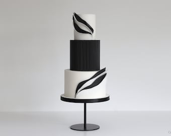 May include: A three-tiered wedding cake with black and white fondant. The bottom tier is white with black abstract designs. The middle tier is black with vertical lines. The top tier is white with black abstract designs.
