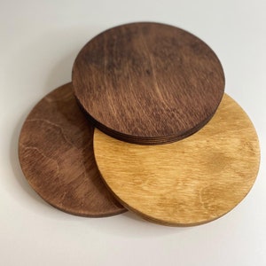 May include: Three round wooden coasters, one is light brown, one is dark brown, and one is a medium brown. The coasters are stacked on top of each other.