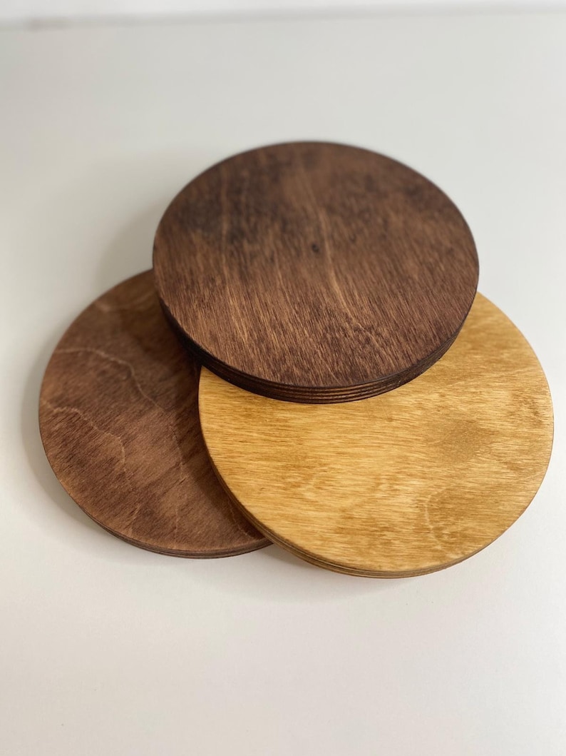 May include: Three round wooden coasters, one is light brown, one is dark brown, and one is a medium brown. The coasters are stacked on top of each other.