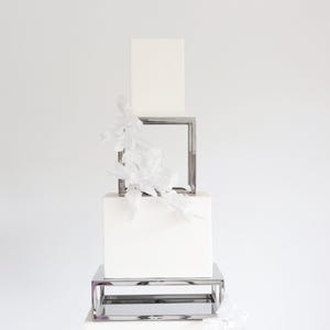 May include: A three-tiered white cake stand with a silver frame. The cake stand is decorated with white flowers.