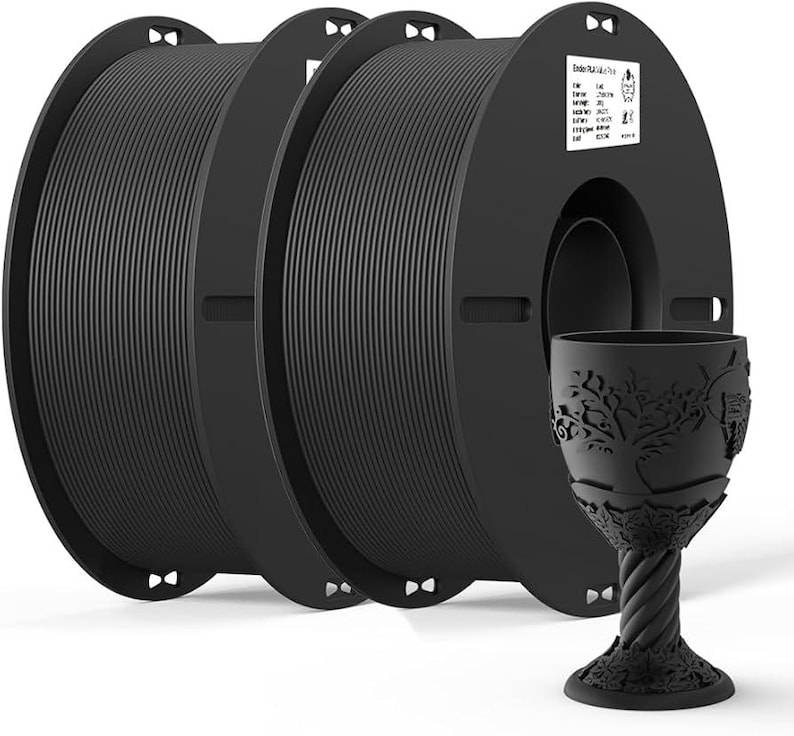 May include: Three spools of black filament for 3D printing. The filament is wound around a black plastic spool with a label that reads "Ender 3 Pro". A black plastic goblet with a tree design is in the foreground.