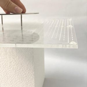 Peut inclure: Un plateau tournant à gâteau en acrylique transparent avec un motif quadrillé et une base en métal. Le plateau tournant est sur une base en mousse blanche.