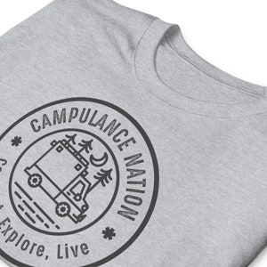 K&ouml;nnte beinhalten: Ein graues T-Shirt mit einer schwarz-wei&szlig;en Grafik eines Wohnmobils mit B&auml;umen und einer Mondsichel. Die Grafik befindet sich in einem Kreis mit dem Text "Campulance Nation" darum herum. Der Text "Explore, Live" befindet sich unter dem Kreis.